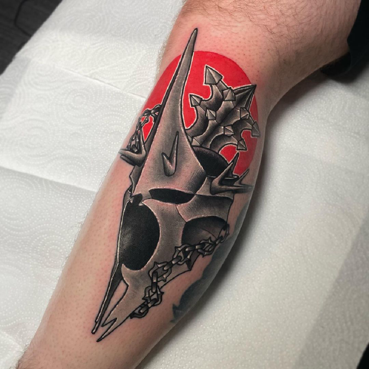 A neo-traditional tattoo by Peter Murray showing the Witch-king's helmet and flail on a red circle.