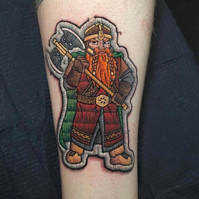 A patchwork style tattoo by Duda Lozano featuring Gimli the dwarf and his axe.