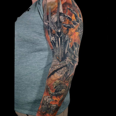 A colour realism full sleeve tattoo by Nick Noonan featuring Saurman, some orcs and Grond on a battlefield