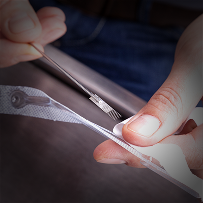 A flat tattoo needle being taken out of packaging.