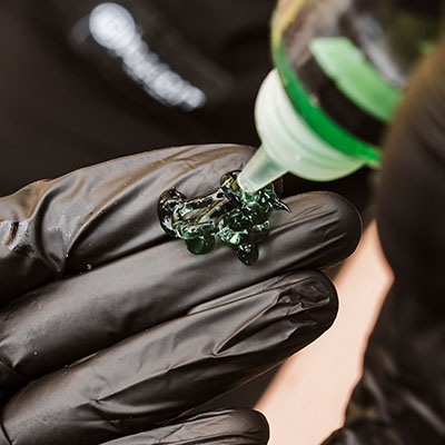 Ein Tätowierer trägt Tattoo-Schablonenprimer auf seine Hand auf und trägt dabei schwarze Nitrilhandschuhe.